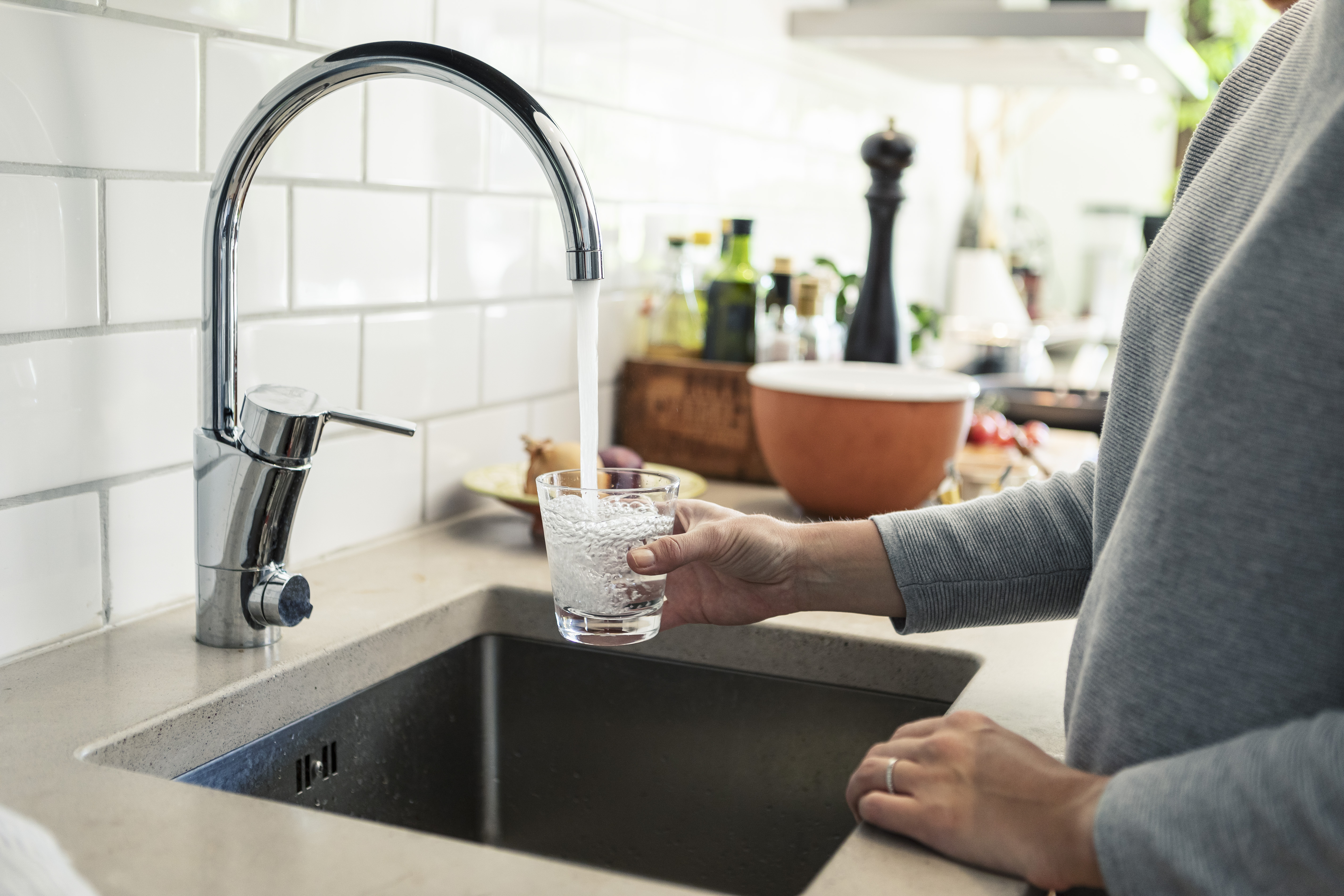 woman holding glass under faucet in kitchen